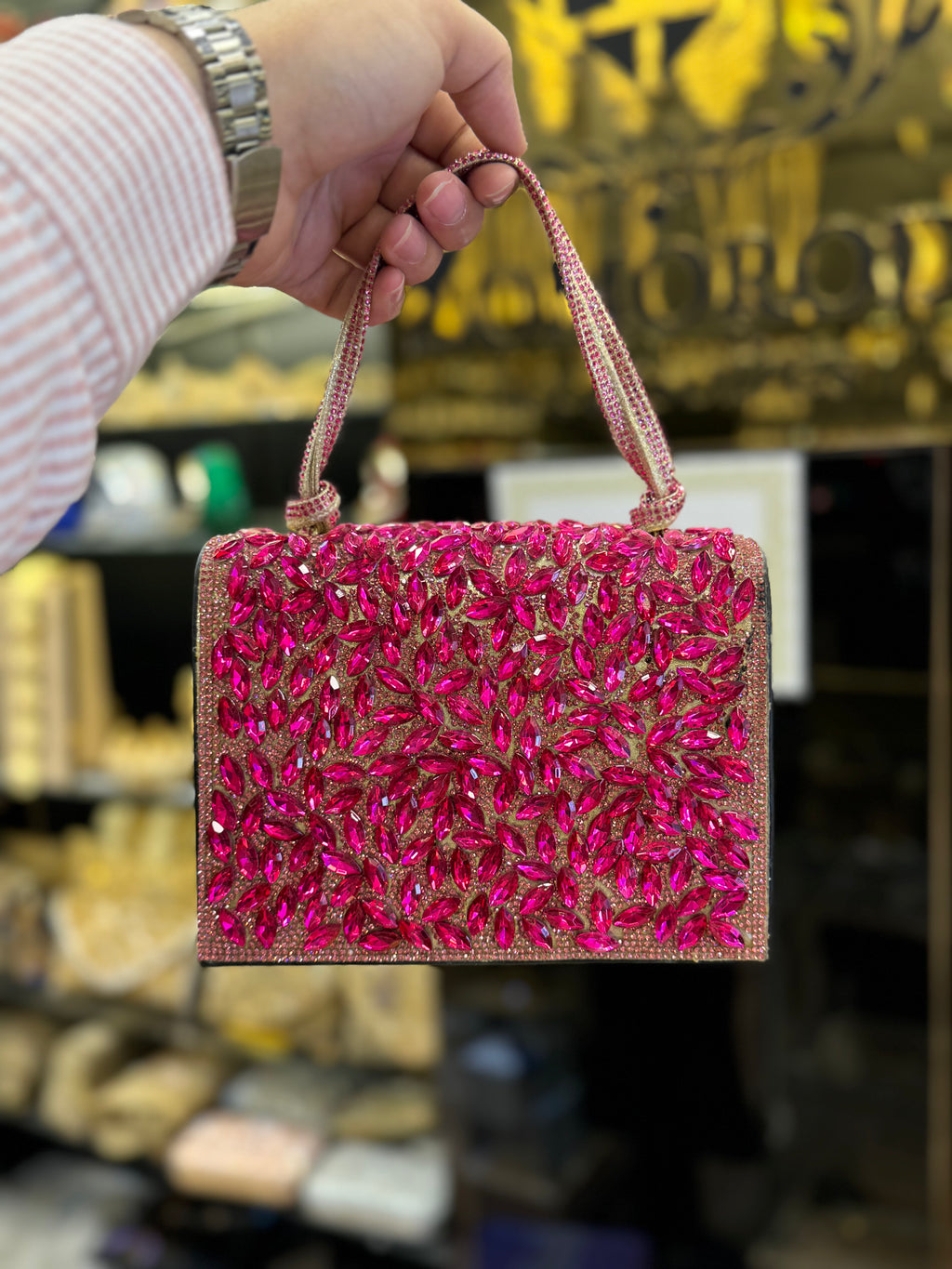 Hand holding a pink beaded handbag with a blurred store background