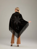 Person wearing a black shawl with intricate designs in a minimal indoor setting.
