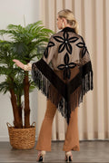 Woman wearing a patterned shawl with fringe, standing indoors next to a plant.