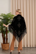 Woman wearing a black embroidered shawl with fringes in an indoor setting.