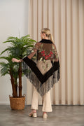 Woman wearing a decorative shawl with fringe in a room with a plant and curtain.