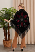 Woman wearing a black poncho with red floral patterns and fringe, standing indoors.