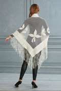Woman wearing a gray and white patterned poncho with fringes, standing against a plain background.